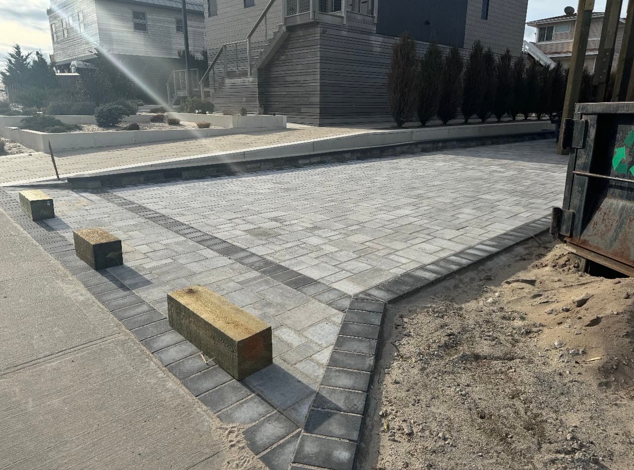 A large paver driveway laid in a running bond pattern with a contrasting charcoal border course, nearing completion.